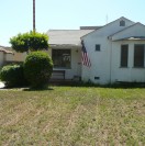A small white house with an American flag and a trimmed bush in front.